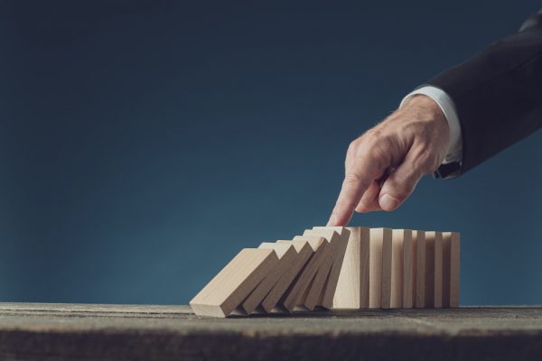 Business crisis manager stopping collapsing dominos with his finger